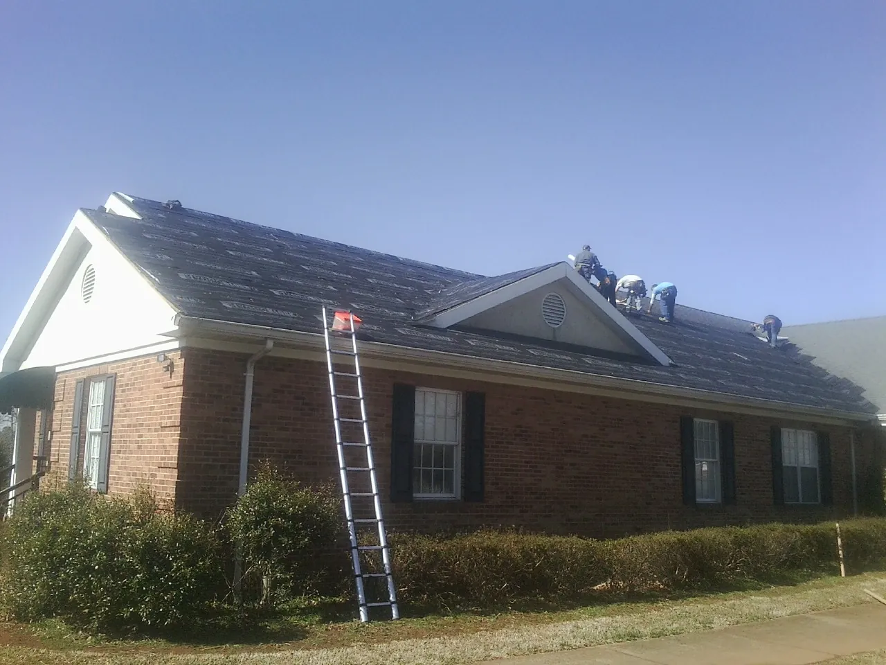 Crew tearing shingles off a brick ranch roof with a ladder set — Emergency Roof Repair work by our crew in Ruther Glen