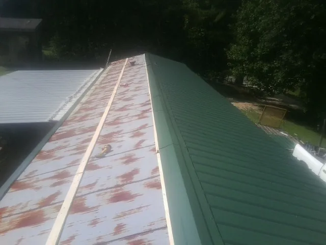 Old rusted panels beside newly installed green metal roofing — Wind Damage Roof Repair by Roofing Brothers in Ruther Glen
