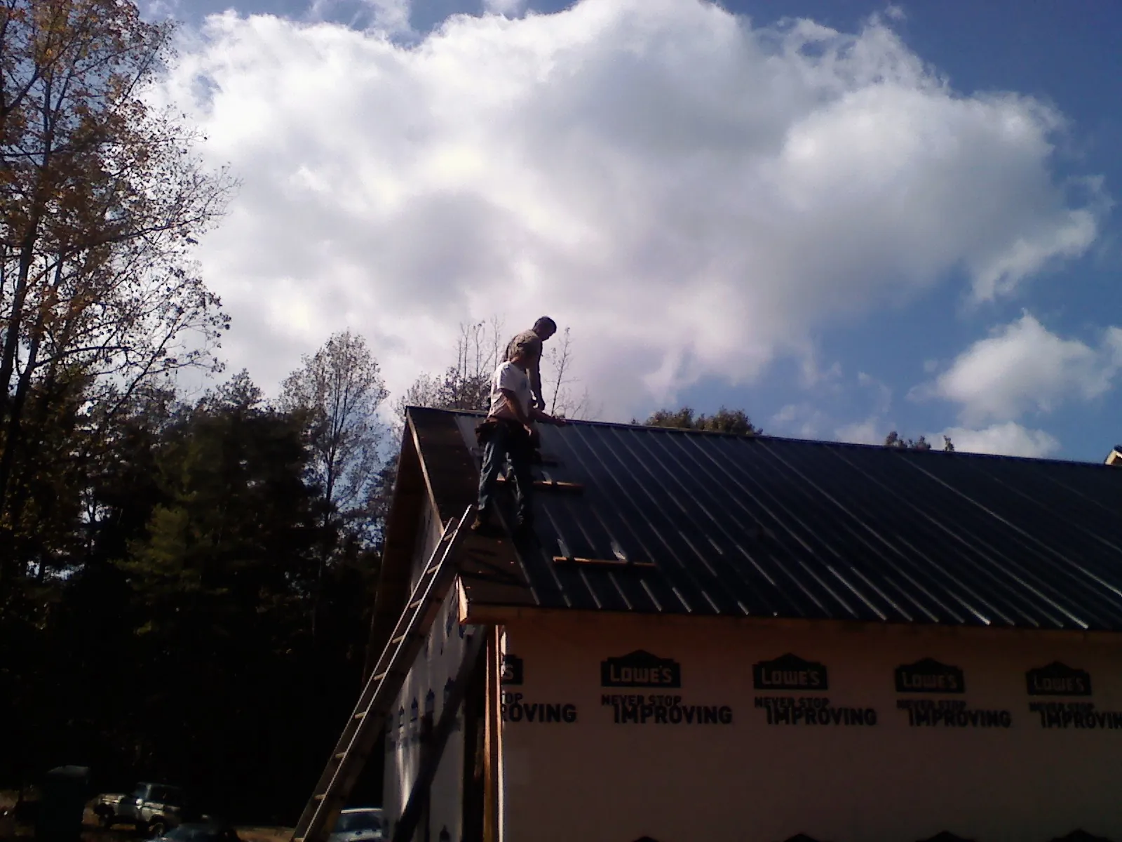 Roofer fastening dark metal panels high against a cloudy sky, from a Roof Inspection job in Ruther Glen