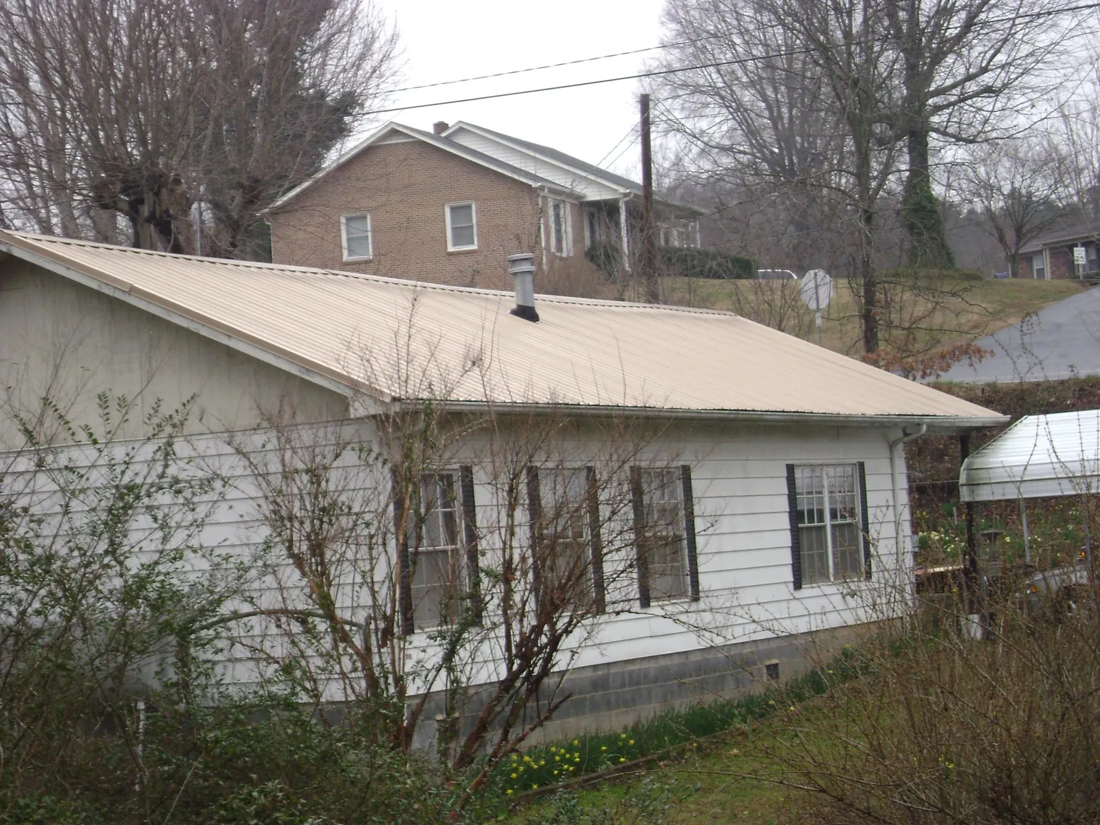 Tan metal roof on a white sided house set into a hillside — Commercial Roofing by Roofing Brothers in Ruther Glen