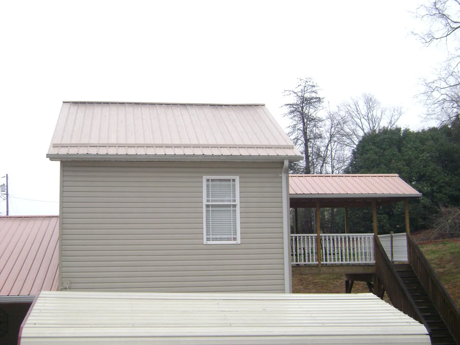 Tan metal roofs on a two story addition and attached porch, from a Roof Replacement job in Ruther Glen